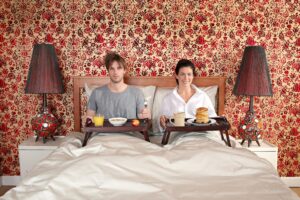 A man and a woman sitting in a bed having breakfast.