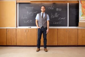 A teacher standing in front of classroom with a chalkboard behind him.