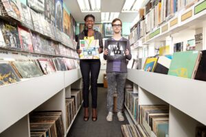 A man and woman holding up a vinyl record each in a record shop.