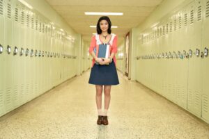 A femail student standing in an empty hallway holding her books.